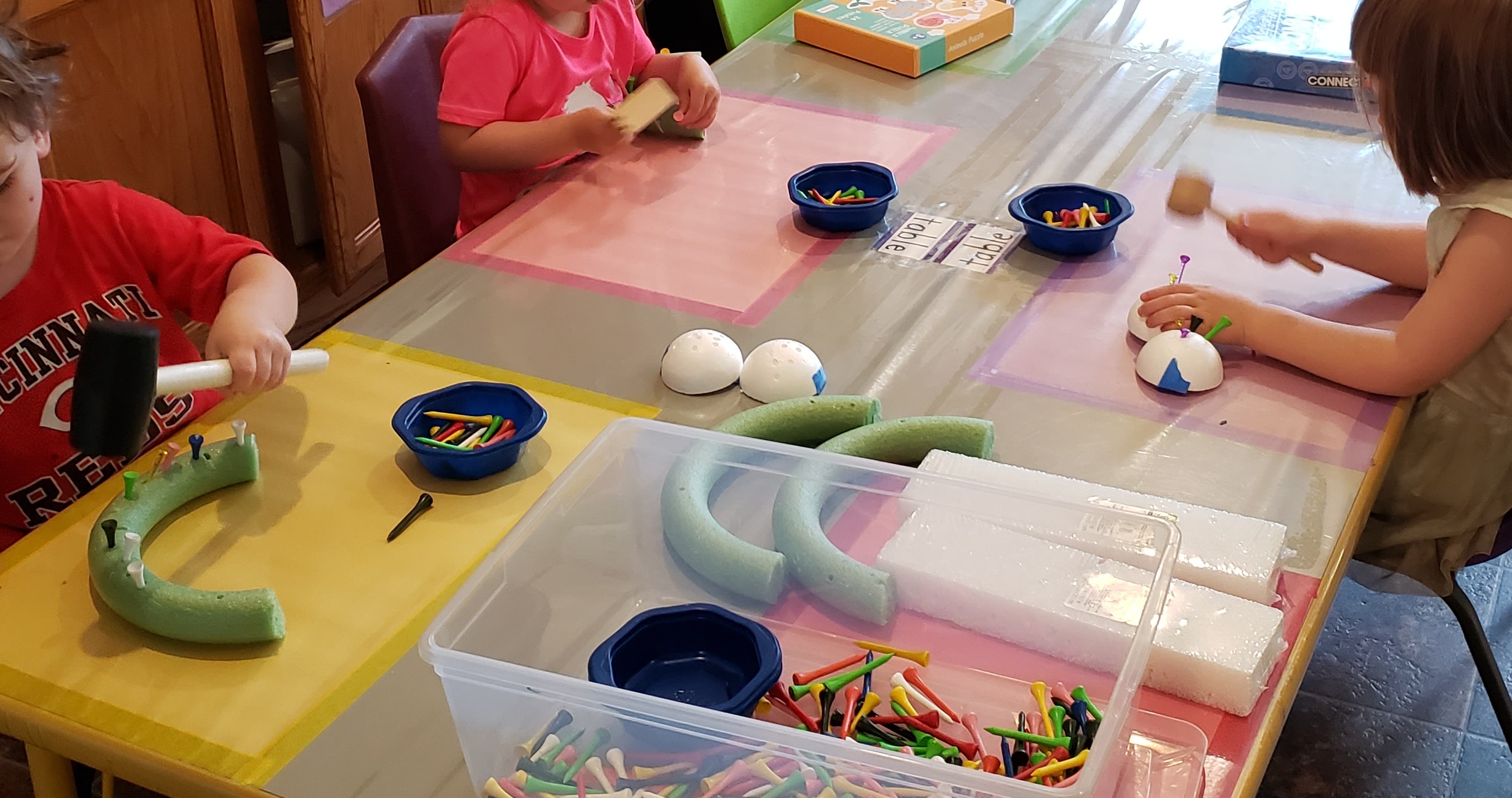 Photo. Three small children playing with foam, toy mallets, and plastic pegs.