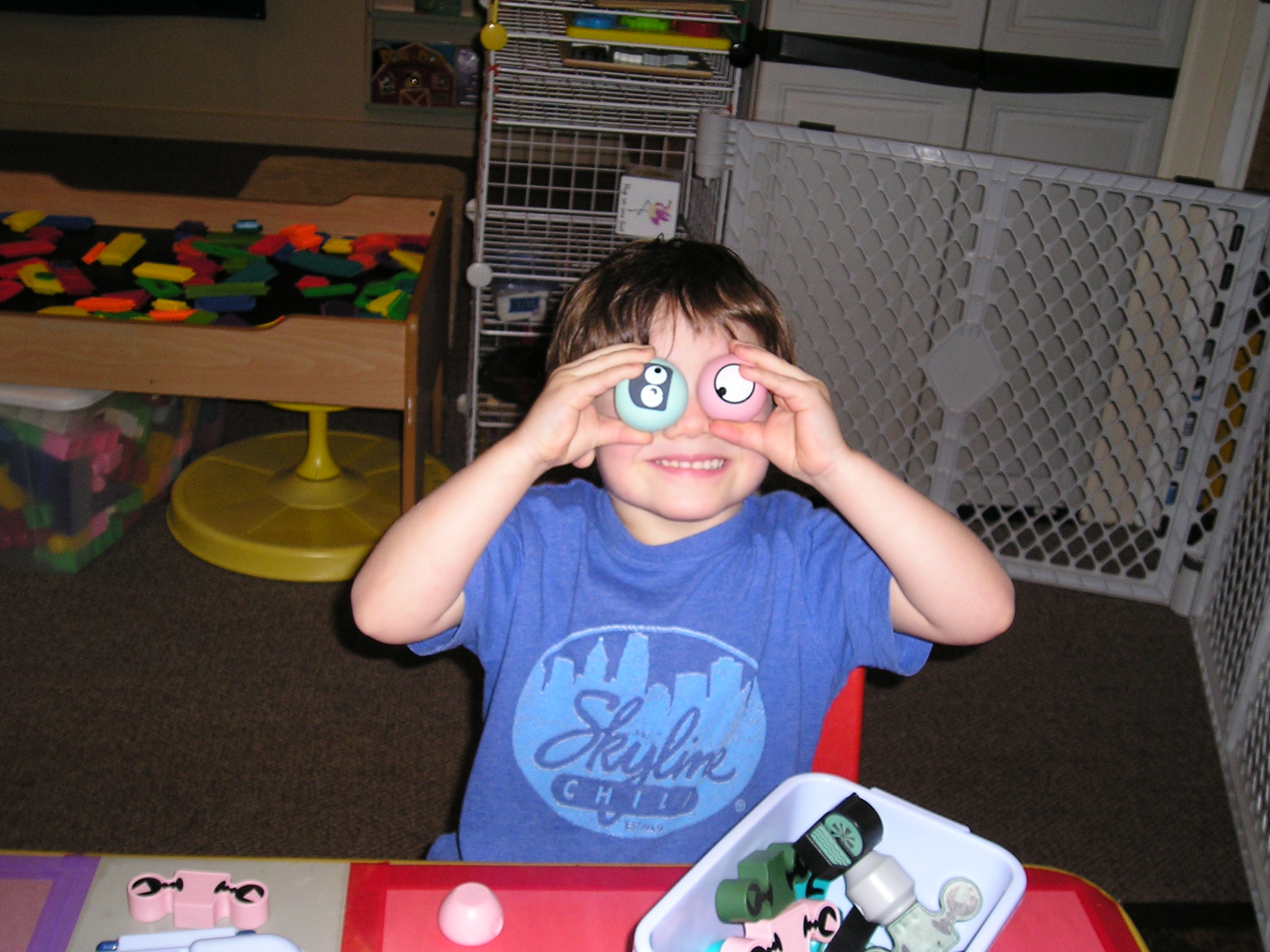 Photo. A small child grinning at the camera and holding up ping-pong balls in front of his eyes.
