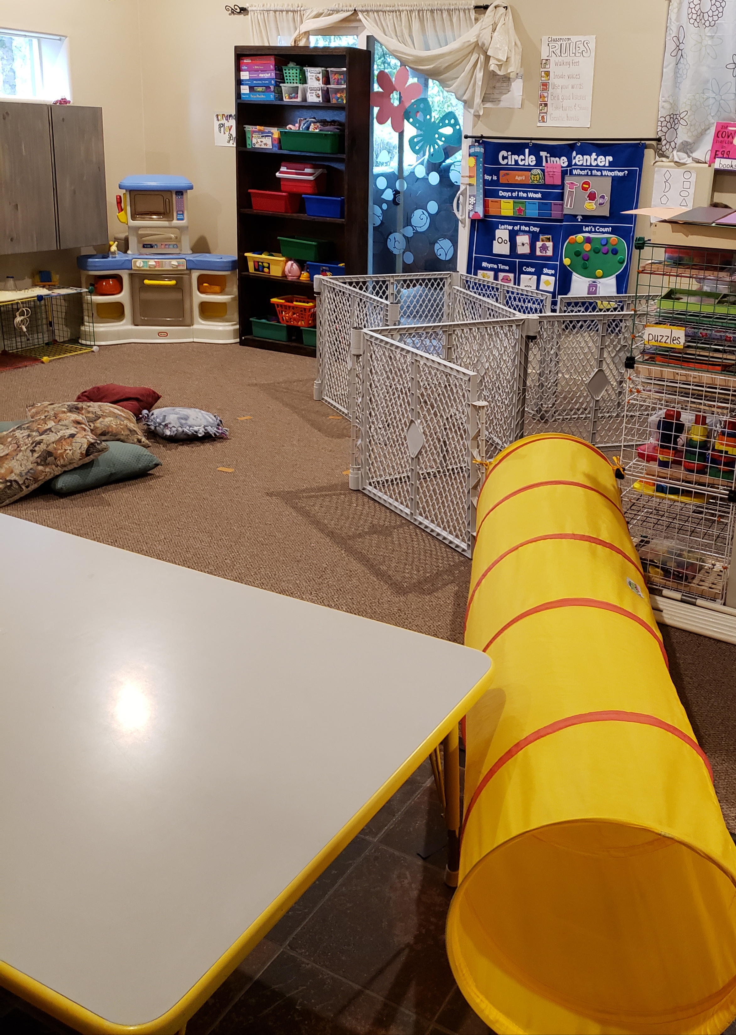 Photo. The empty playroom. There are toys, puzzles, posters, and a small pile of pillows.