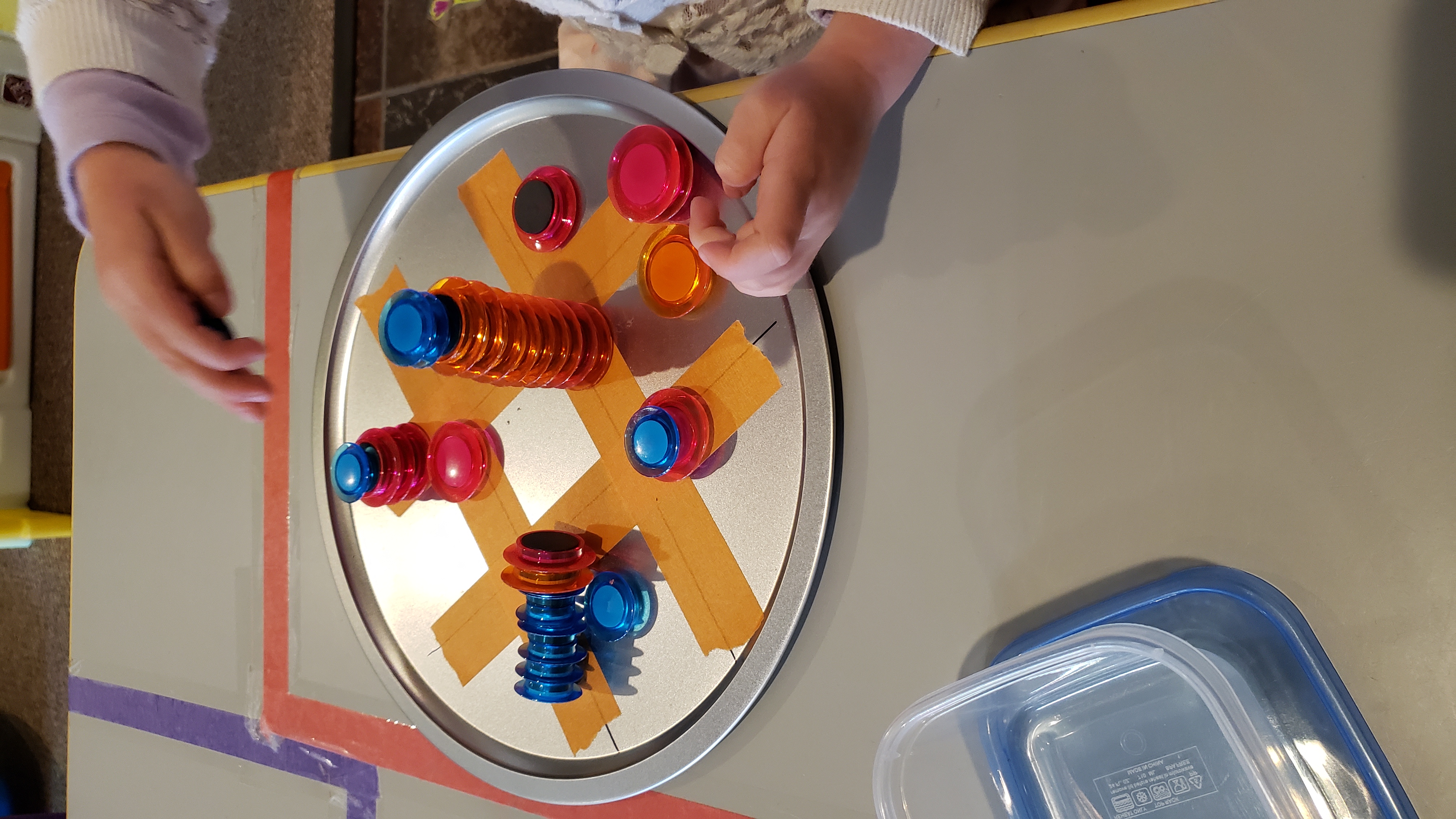 Photo. A small game of tic-tac-toe, played with colorful disc-shaped magnets.